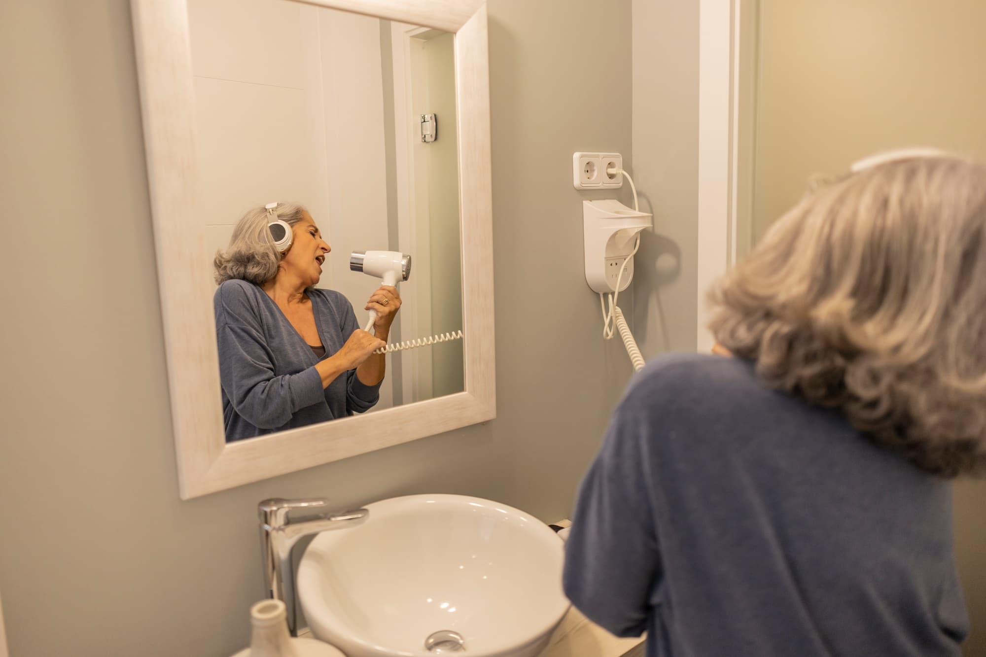 Portrait of senior woman wearing headphones and bathrobe indoors at home.