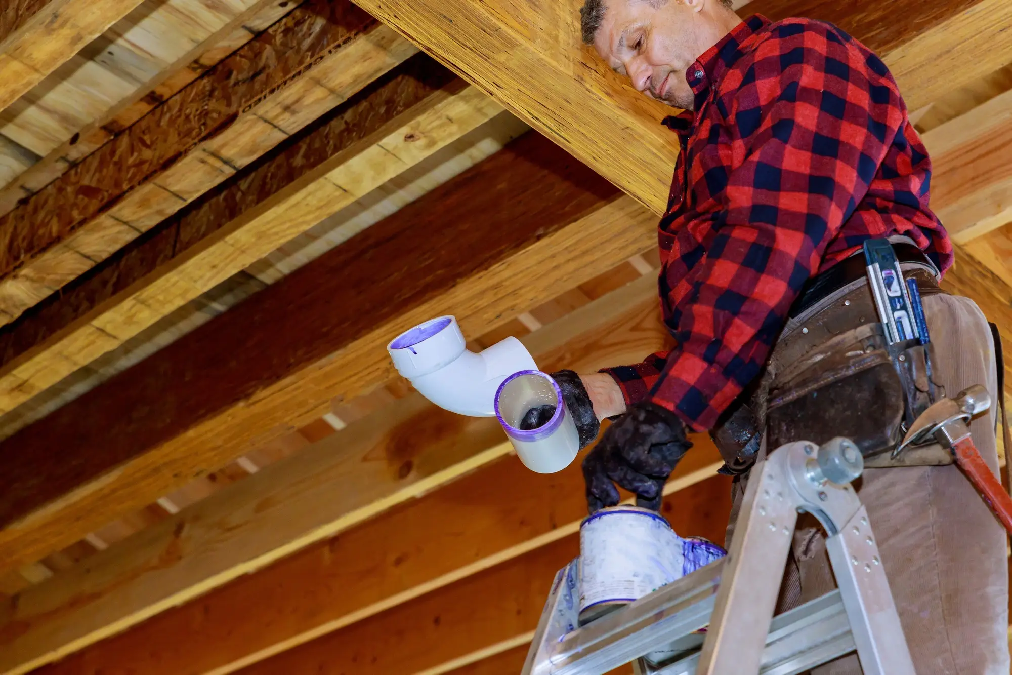 Plombier en train d’installer un tuyau en PVC sous une charpente en bois
