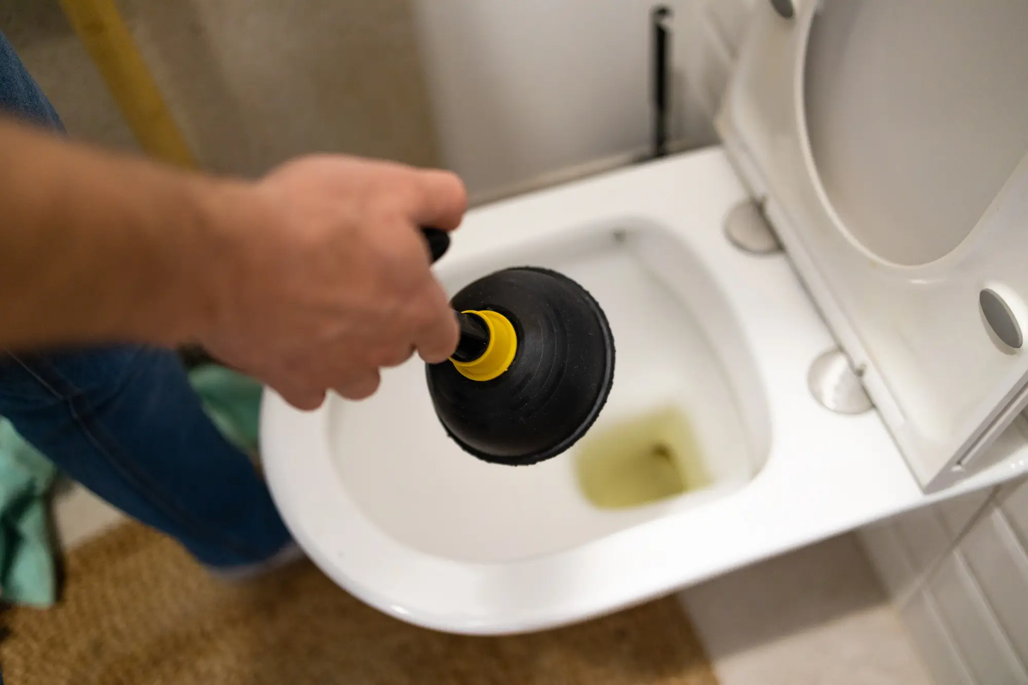 Serviceman repairing toilet with hand plunger. Clogged toilet.